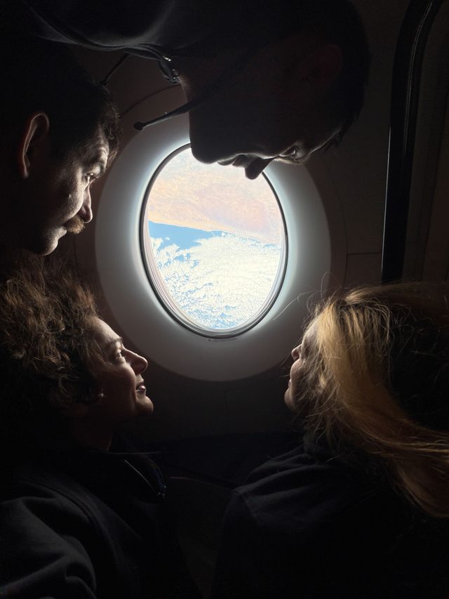 NASA’s SpaceX Crew-12 crew members surround an oval-shaped window aboard a SpaceX Dragon, looking out at clouds above blue water and a tan landmass. From the left, rotating clockwise around the image are NASA astronaut Jack Hathaway, Roscosmos cosmonaut Andrey Fedyaev, ESA (European Space Agency) as